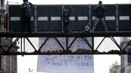   Dos hombres protestan arriba de un pórtico sobre Alameda de Santiago 